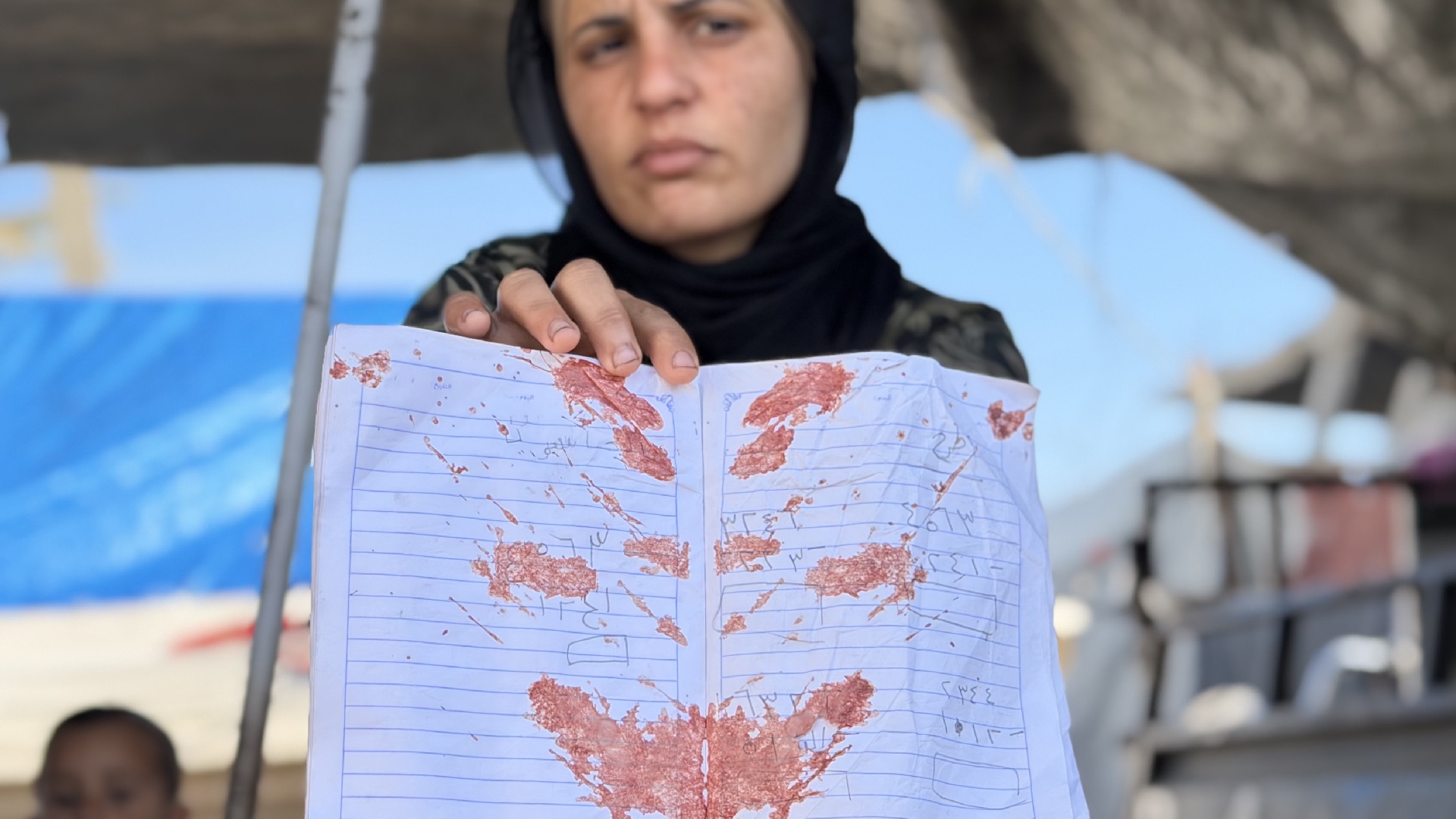 Ola Rihan holds the bloodstained notebook of her daughter, Ritaj Abdulrahman Rihan, who was killed by Israeli fire while solving a maths question